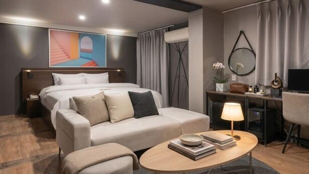 A modern hotel room with a bed, sofa, coffee table, and a desk with a lamp. - Urban HOTEL&PLAY (Seoul)