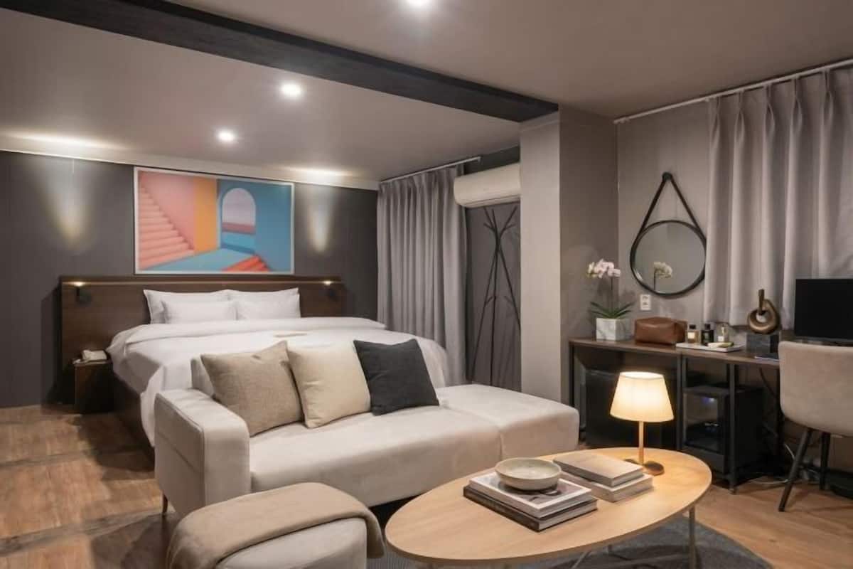A modern hotel room with a bed, sofa, coffee table, and a desk with a lamp.