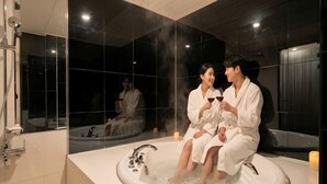 A modern bathroom with a large bathtub, a shower area, and a mirror reflecting the room. - Urban HOTEL&PLAY (Seoul)
