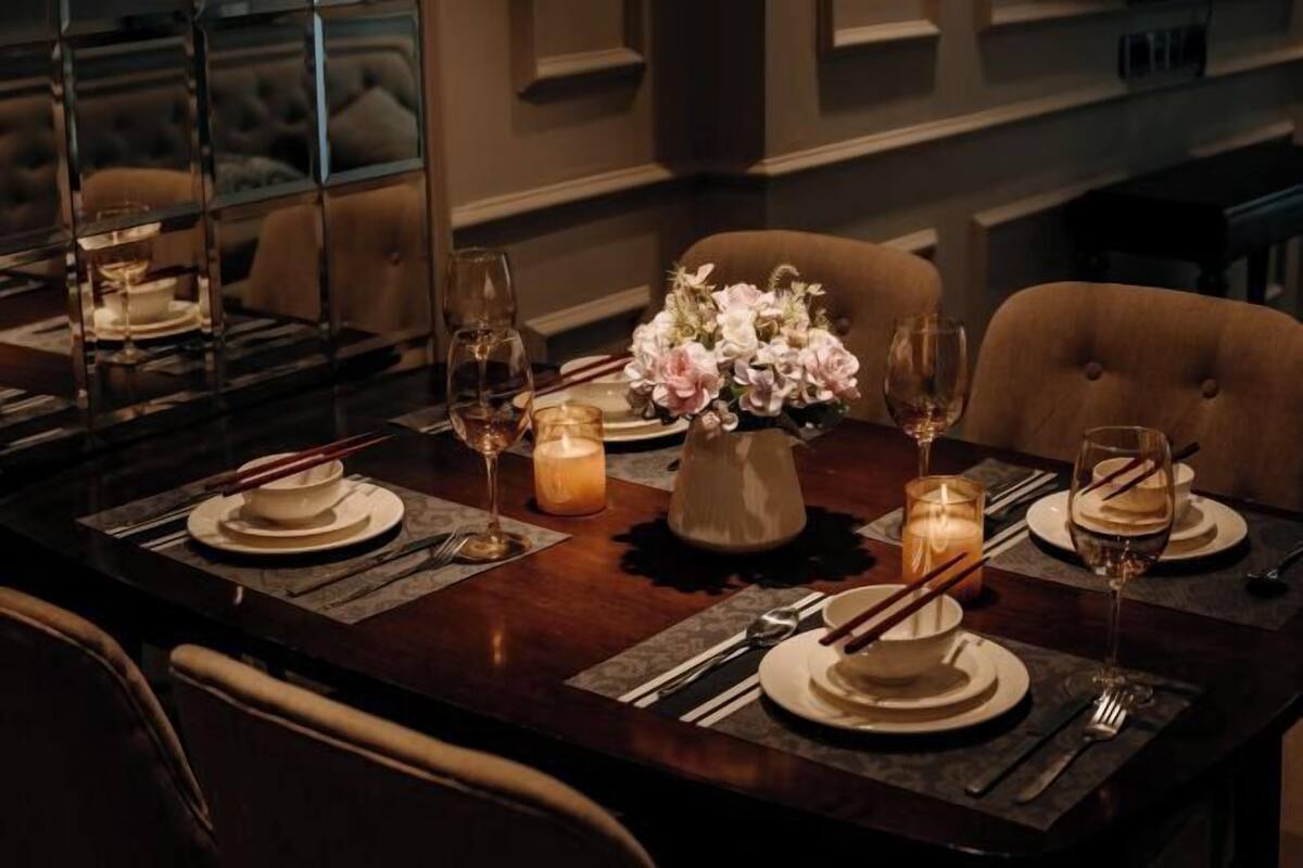 A dining table set with plates, glasses, chopsticks, and candles, with a vase of flowers in the center.