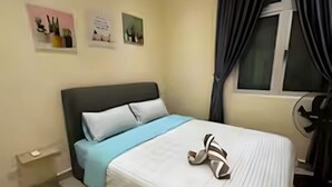 A neatly made bed with a blue bedspread and a pair of shoes on it. There are two pillows, one white and one gray. The room has a window with curtains, a small shelf with plants, and a picture on the wall. - Meridin Bayvue (Plentong)
