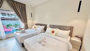 A hotel room with two beds, a small table, a nightstand, and a view of a pool with a flamingo statue. - HH Villa Private Pool Bercham (Ipoh)