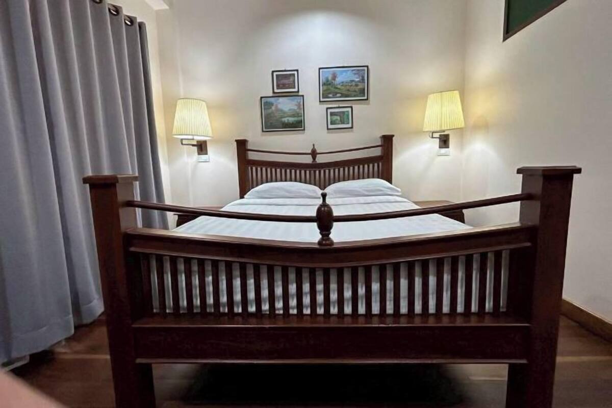 A wooden bed with a headboard, two wall-mounted lamps, and three framed pictures on the wall.