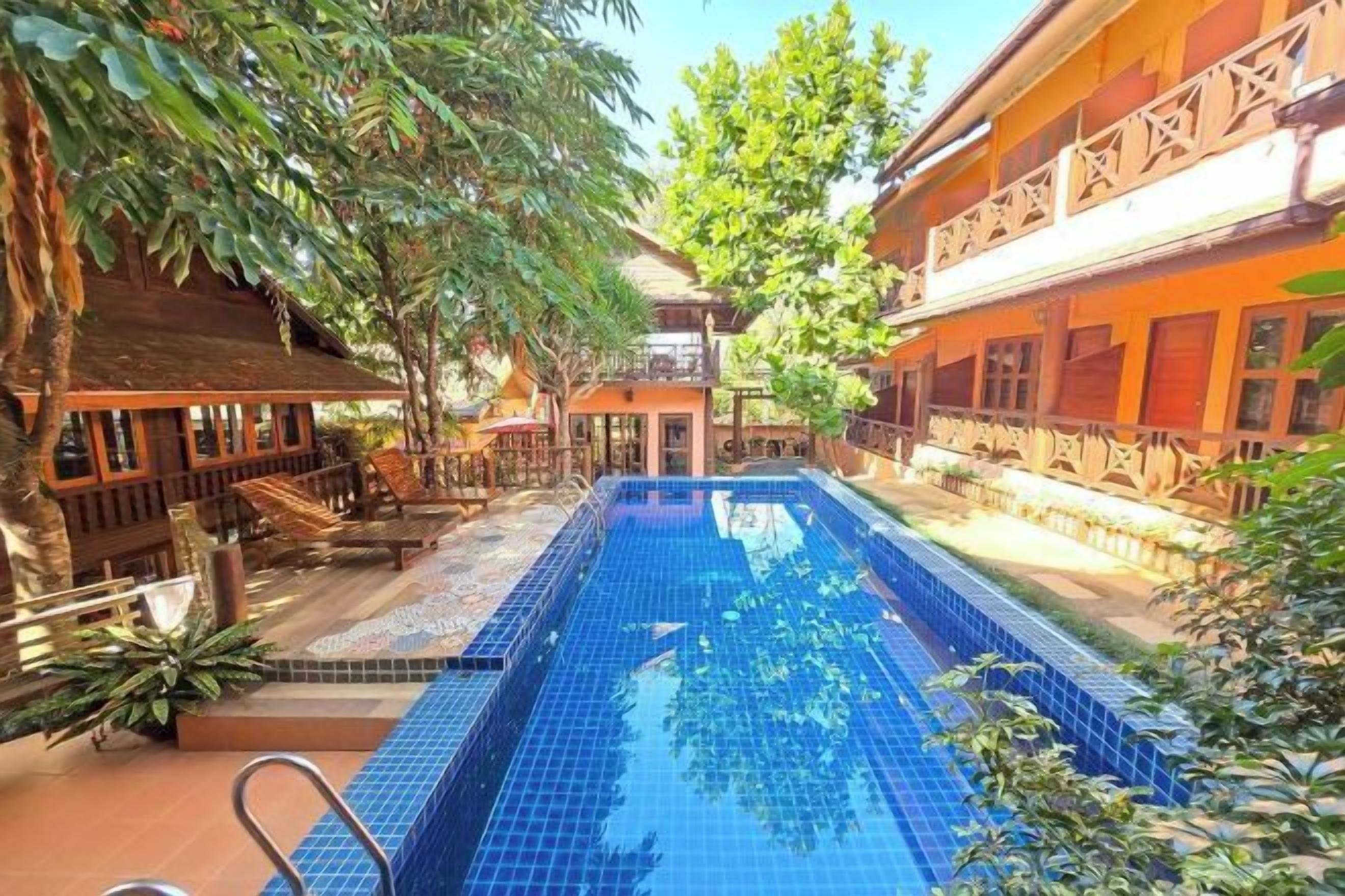 A swimming pool surrounded by buildings with balconies, trees, and outdoor seating areas.