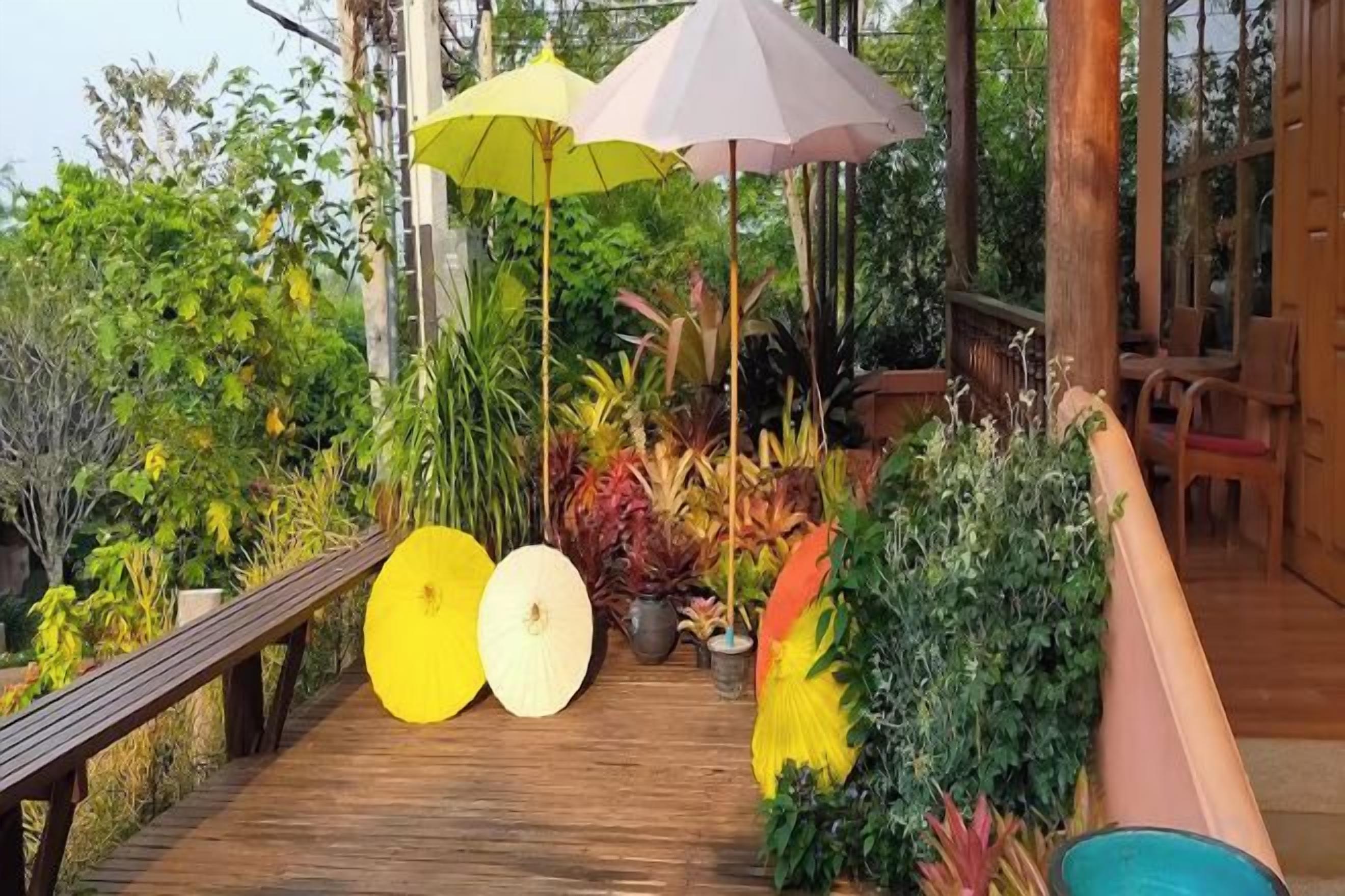 A wooden deck with potted plants and umbrellas, leading to a covered area with seating.