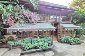 A covered outdoor seating area with a wooden structure, surrounded by potted plants and a balcony. - Baan Yung Hill Resort (Chiang Rai)