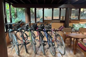 A room with bicycles parked against the wall, a wooden table, and a window with a view of greenery. - Baan Yung Hill Resort (Chiang Rai)