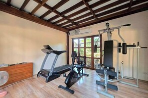 A gym with a treadmill, elliptical, and weight machines, wooden floor, and large windows. - Baan Yung Hill Resort (Chiang Rai)
