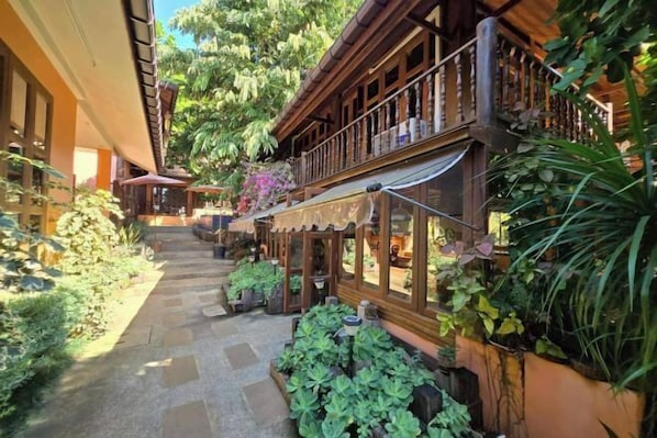 A courtyard with a wooden building, stone pathway, and lush greenery.