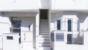 A two-story building with a white exterior, a front door, and a staircase leading to the second floor. - Etoile Soshigaya Okura by Tranova (Tokyo)
