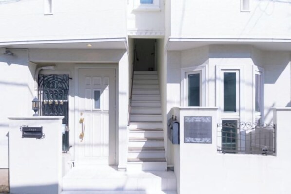 A two-story building with a white exterior, a front door, and a staircase leading to the second floor. - Etoile Soshigaya Okura by Tranova (Tokyo)