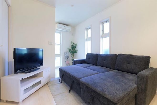 Un soggiorno con una TV a schermo piatto su un mobile bianco, un divano componibile grigio e una pianta in vaso.