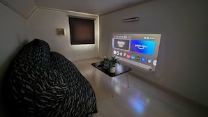 A living room with a sofa, a coffee table with a plant, and a wall-mounted projector displaying an interface. - Etoile Soshigaya Okura by Tranova (Tokyo)