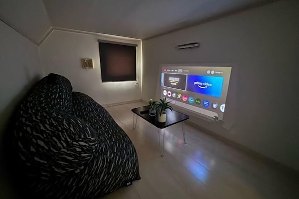 A living room with a sofa, a coffee table with a plant, and a wall-mounted projector displaying an interface. - Etoile Soshigaya Okura by Tranova (Tokyo)