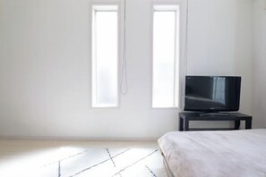 A bedroom with a bed, a TV on a stand, and two windows. - Etoile Soshigaya Okura by Tranova (Tokyo)