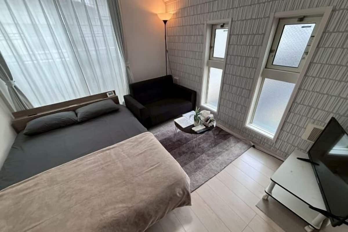 Una habitación con una cama, un sofá, una mesita con una lámpara y un televisor sobre un mueble.
