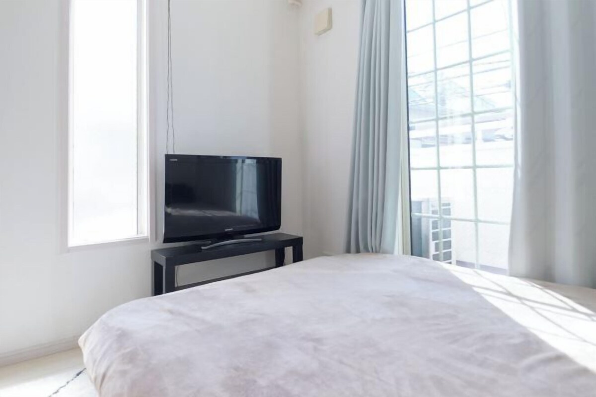 A bedroom with a bed, a TV on a stand, and a large window with curtains.