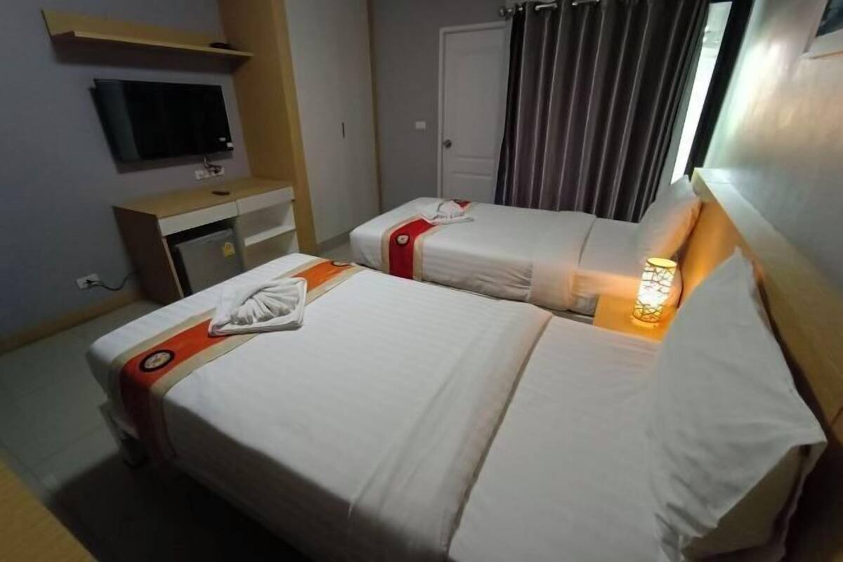 Una habitación de hotel con dos camas, un televisor, un escritorio y una ventana con cortinas.
