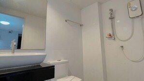 A bathroom with a white sink, black countertop, white toilet, and a shower with a handheld showerhead. - Big Zen Hotel (Nonthaburi)