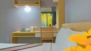 A hotel room with a bed, a desk, a chair, a mirror, and a window with a view of trees. - Big Zen Hotel (Nonthaburi)
