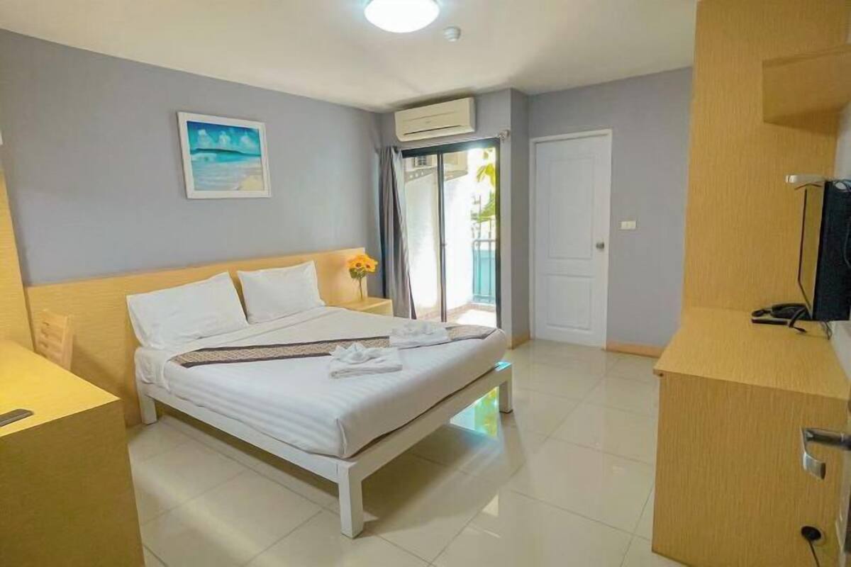 Habitación de hotel con cama, escritorio, silla, televisor y balcón con vistas.