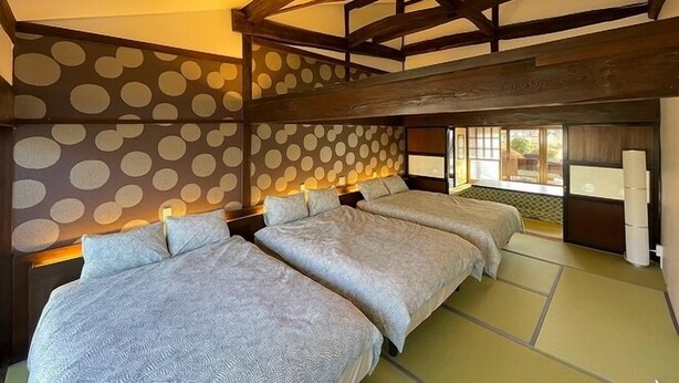 A room with a high ceiling, exposed wooden beams, and a polka dot patterned wall. There are three beds with matching bedding and a small window providing a view. - KandoStay Yatsugatake Fujiyama Terrace (Hokuto)