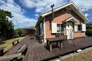 Una terraza de madera con mesas de picnic y un área cubierta, una casa con techo inclinado y una antena parabólica.