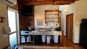 Cocina compacta con horno integrado, pileta y estufa. Una ventana proporciona luz natural, y hay un televisor montado en la pared.