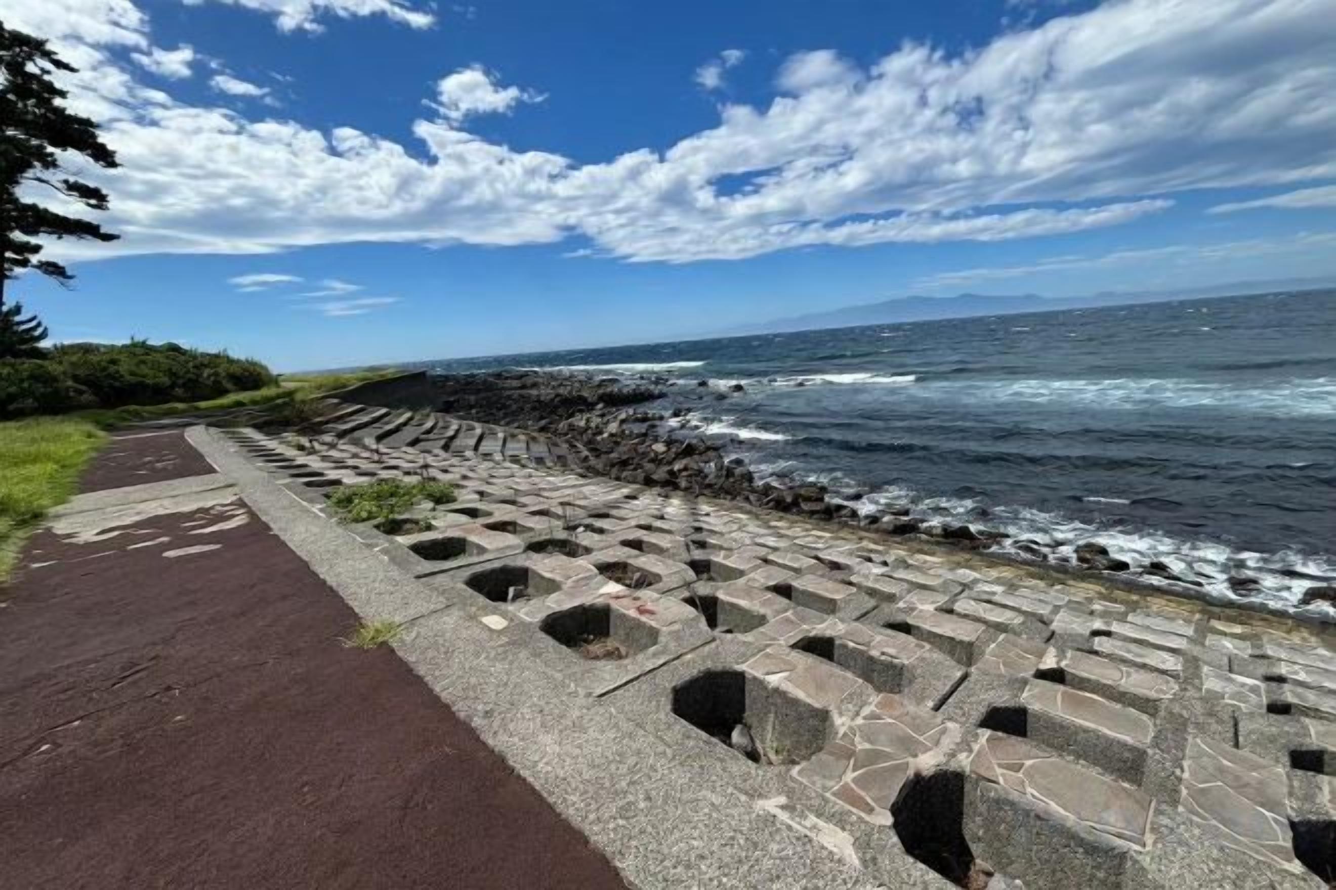 A coastal walkway with a paved path and a stone barrier.