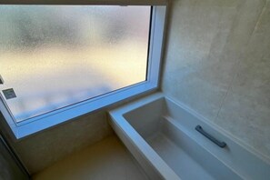 Een badkamer met een bad, een raam en een matglazen deur.