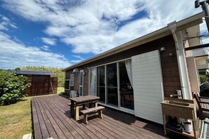 Een overdekt terras met een tafel en bank, een schuifpui en een klein buitenkeuken.
