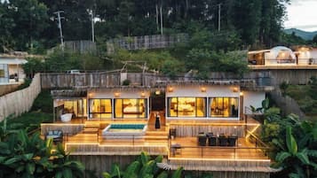 A modern villa with a thatched roof, large windows, and a pool area.