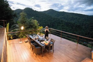 A wooden deck with a dining table and chairs, overlooking a mountainous landscape. - PHULAYYA Chiangmai (Mae Taeng)