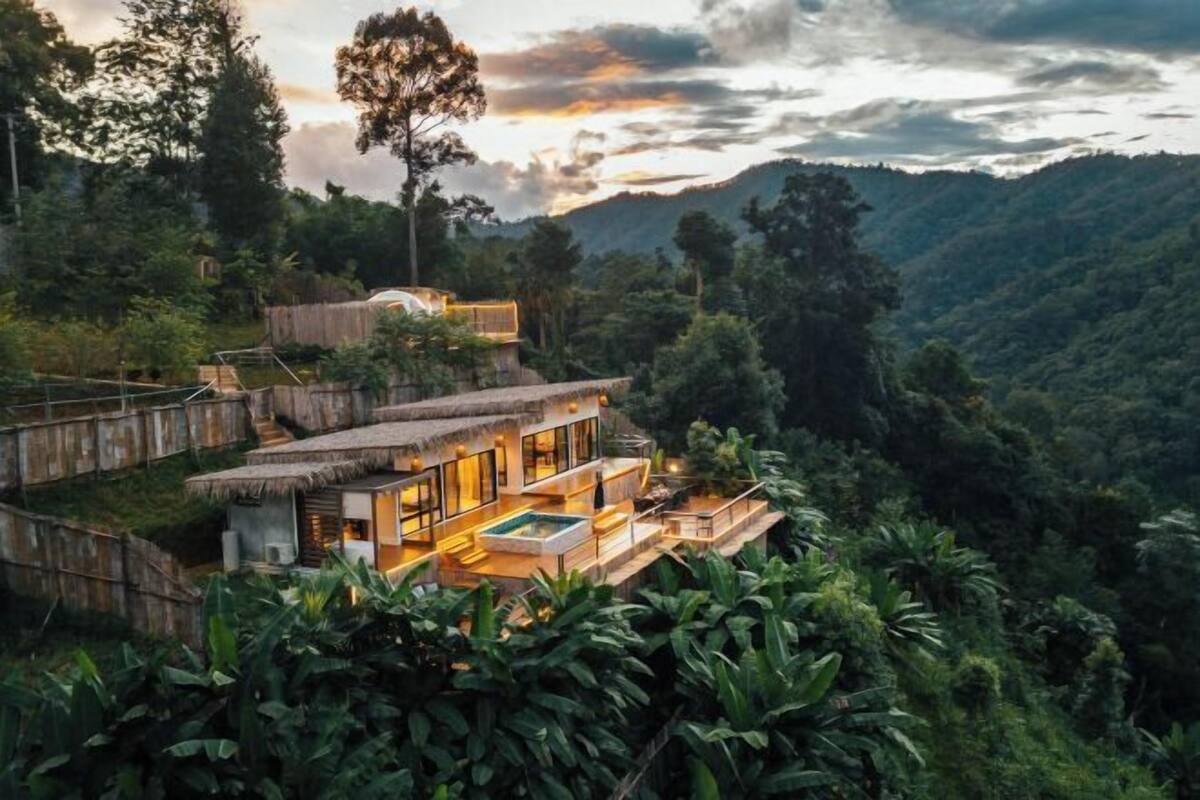 A modern villa with a pool, surrounded by lush greenery and hills.