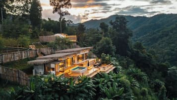 A modern villa with a pool, surrounded by lush greenery and hills.