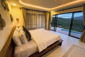 A bedroom with a large bed, a nightstand, and a view of a mountainous landscape through a sliding glass door. - PHULAYYA Chiangmai (Mae Taeng)