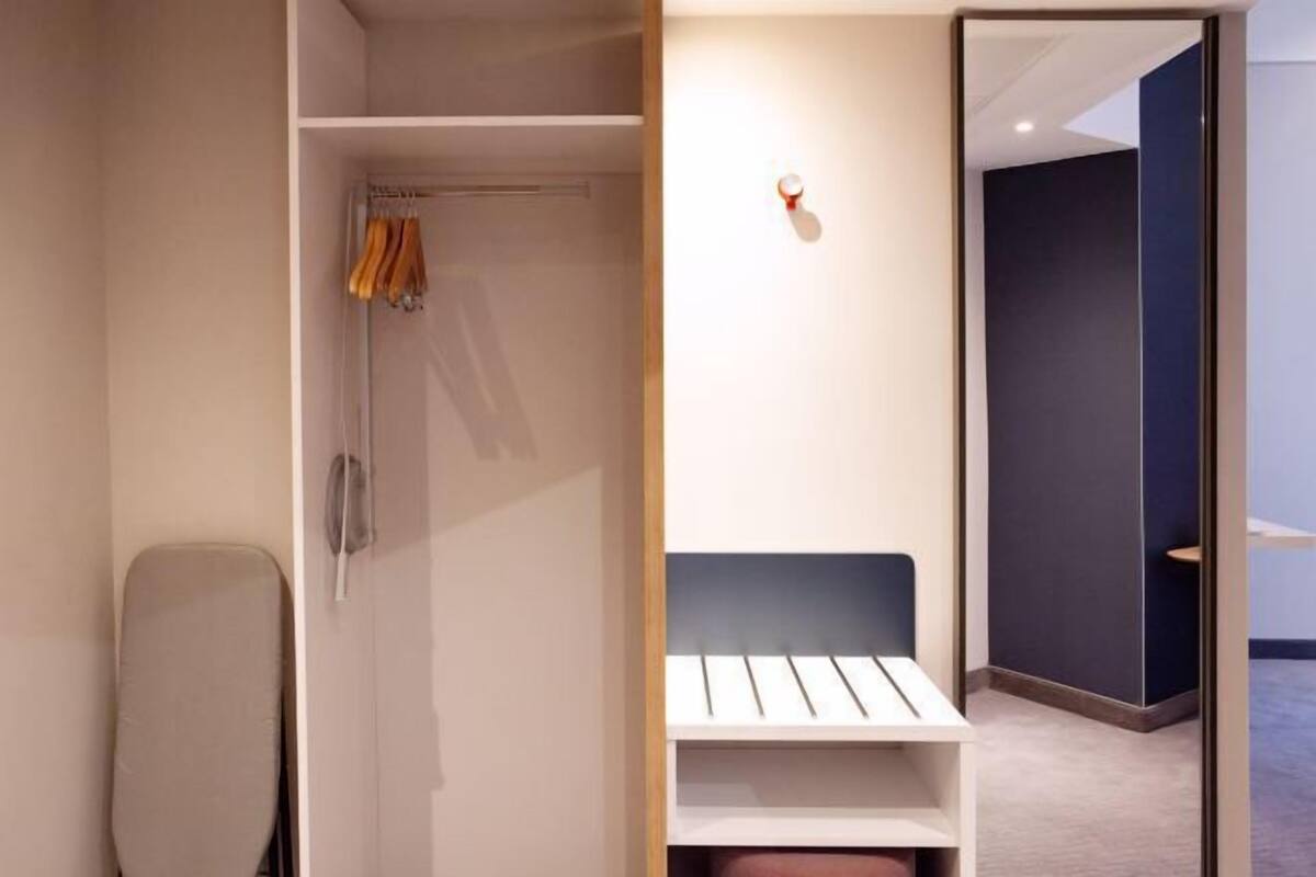 Et moderne værelse med walk-in closet, en seng med sengegavl og en lille reol.