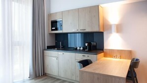 A modern kitchen with wooden cabinets, a microwave, a coffee machine, and a dining area with a table and chairs. - Holiday Inn Express & Suites MONHEIM AM RHEIN by IHG (Bedburg)