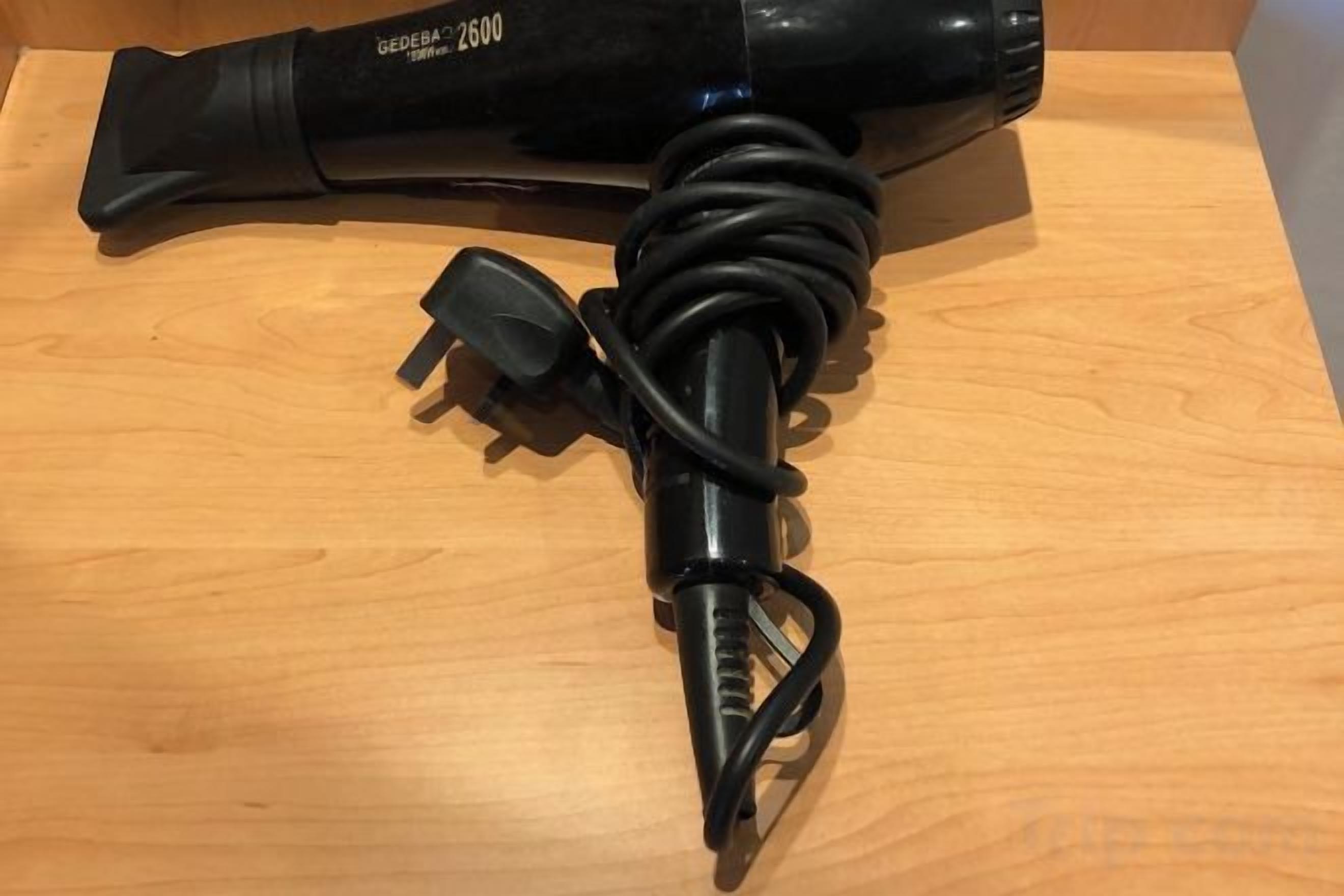 A hair dryer with a coiled cord and a power adapter on a wooden surface.