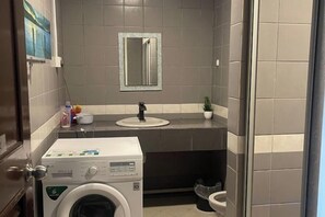 A compact bathroom with a washing machine, a sink, and a toilet. - Riverbank Suites 306 with beautiful RiverView (Kuching)