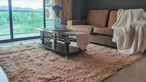 Ein Wohnzimmer mit einer Couch, einem Glastisch und Blick auf Grün hinter großen Fenstern.