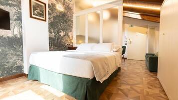Une chambre d’hôtel avec un lit, un couvre-lit vert, un mur orné d’une fresque représentant un arbre, un plancher en bois et une porte donnant sur une autre pièce.