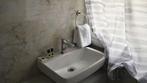A bathroom with a marble wall, a round mirror, a sink with a towel, and a striped shower curtain. - Hotel Gateway Asansol (Asansol)