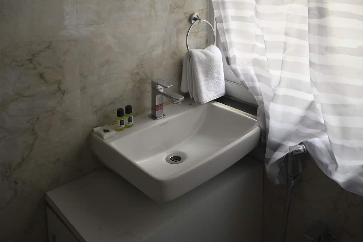 A bathroom with a marble wall, a round mirror, a sink with a towel, and a striped shower curtain.