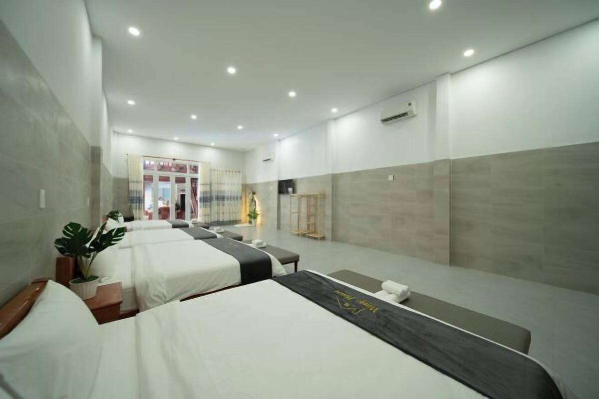 A hotel room with three beds, a large mirror, and a plant.