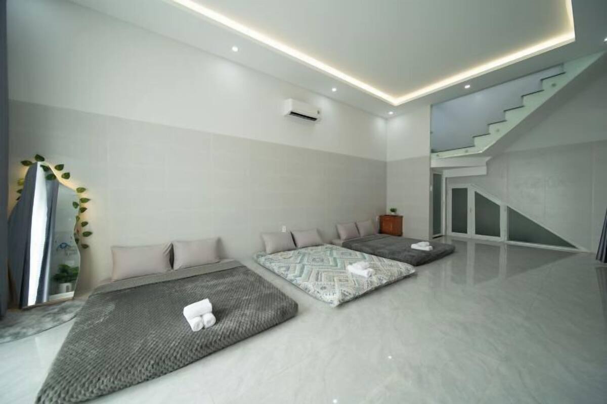 A modern hotel room with a large bed, a seating area, a staircase, and a mirror with a decorative frame.