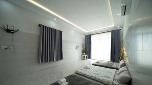 Une chambre d’hôtel moderne équipée d’un lit, d’un petit coin salon, d’une fenêtre avec des rideaux et d’un climatiseur fixé au mur.