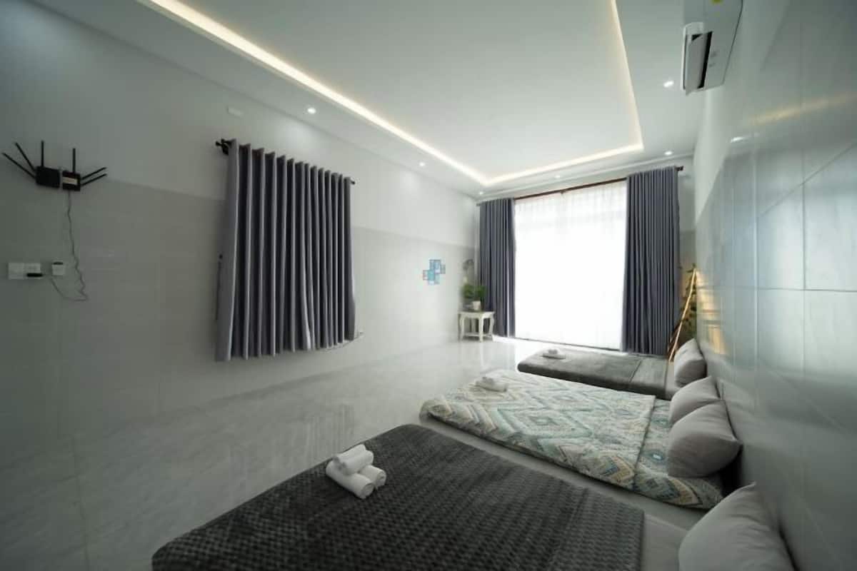 A modern hotel room with a bed, a small seating area, a window with curtains, and a wall-mounted air conditioning unit.