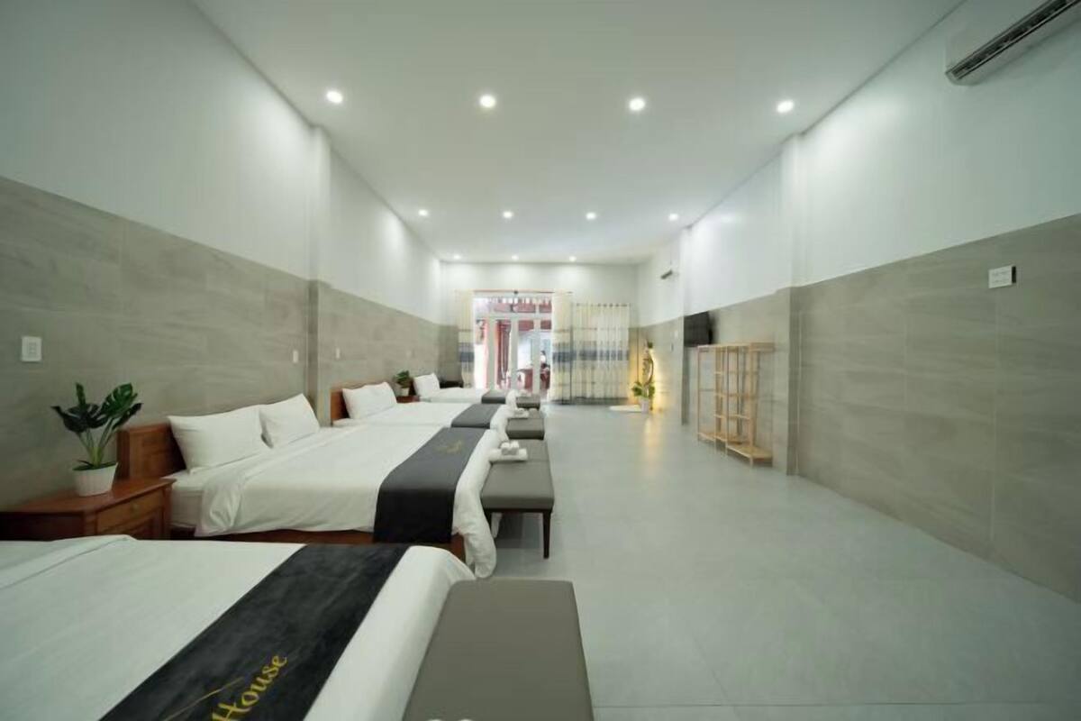 A hotel room with a large bed, a smaller bed, a bench, a plant, and a wooden cabinet.