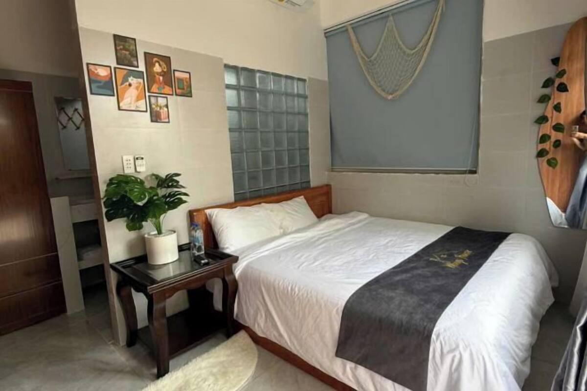 A bedroom with a bed, bedside table, potted plant, and wall art.